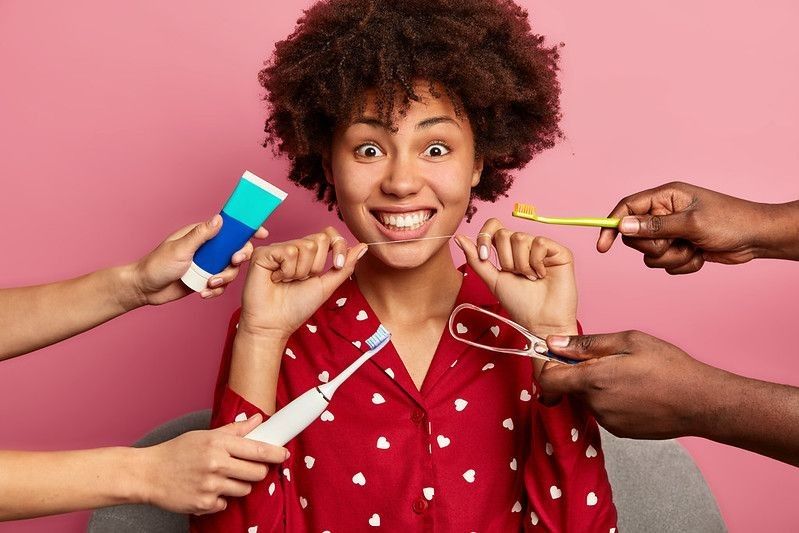 A curly woman cares about teeth, holds dental floss, surrounded by toothpaste and toothbrushes representing national toothache day.