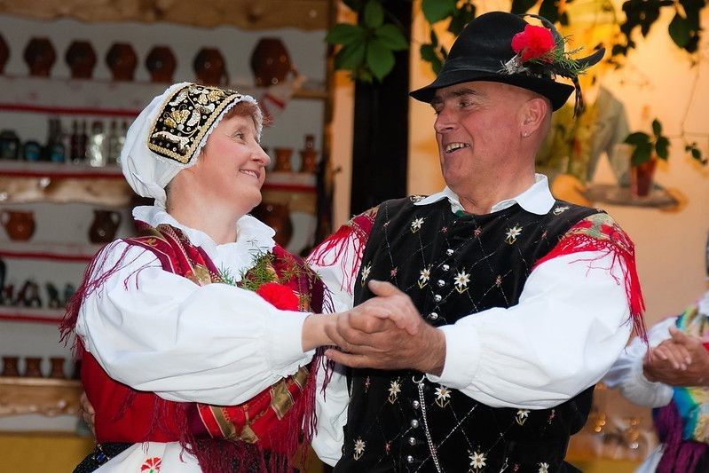 A elderly couple dressed in Gorenjska national costumes dancing polka in the garden in the evening.