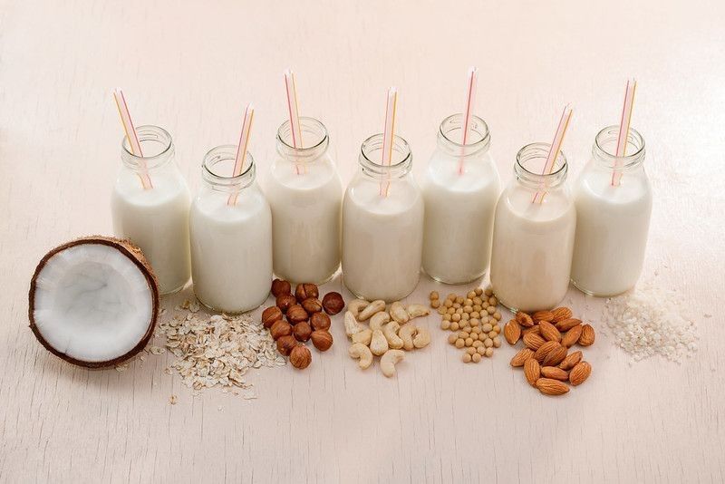 Bottles of assorted vegan milks with straws and ingredients on beige table