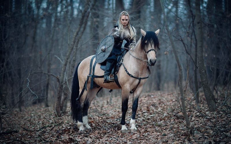 Viking warrior female sitting on a horse in forest.