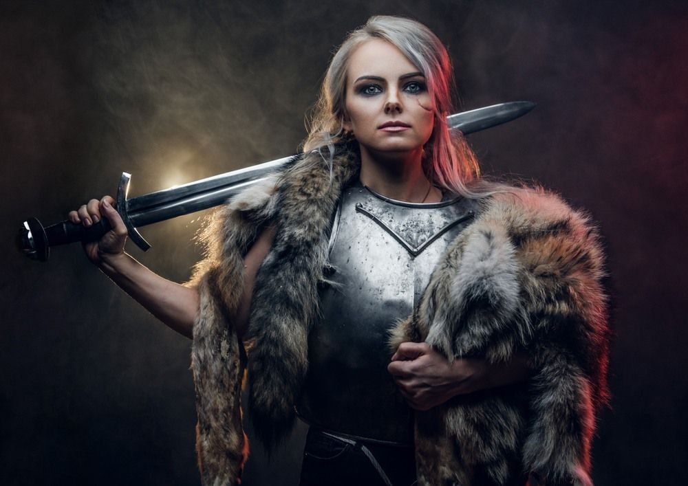 Portrait of a beautiful warrior woman holding a sword wearing steel cuirass and fur.