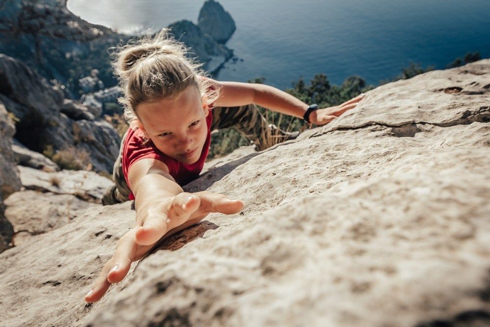 Brave young woman climber fearlessly climbs up sheer stone wall in mountains, overcoming obstacles.