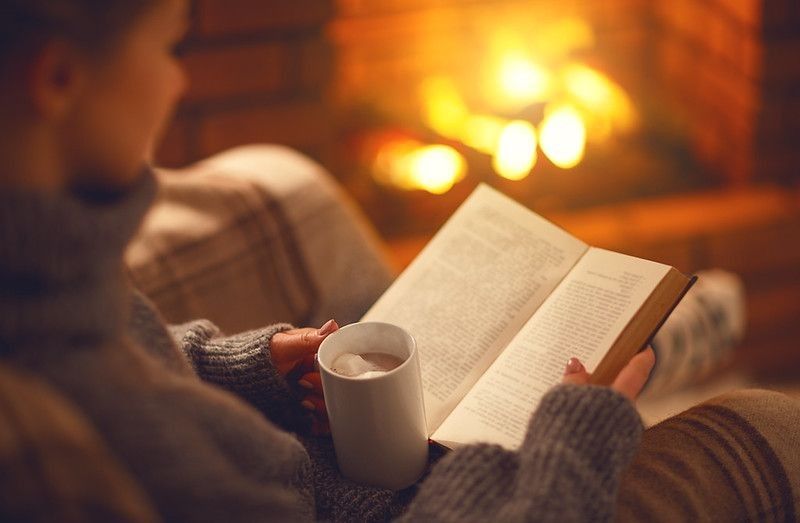A girl reading a book with a cup of coffee near fireplace