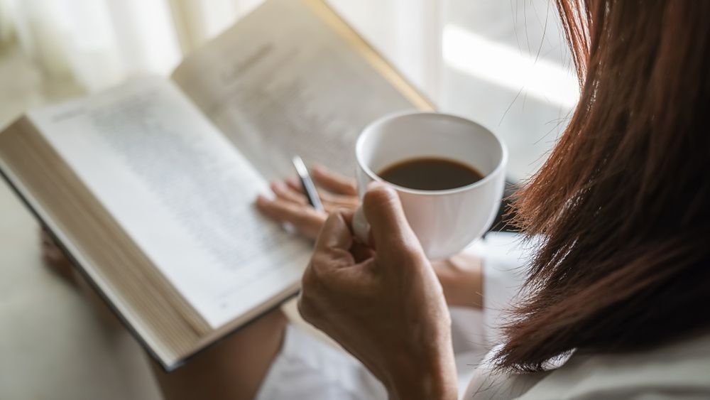 Woman holding a cup of coffee and reading a book