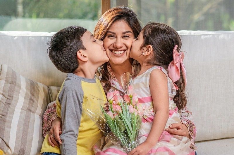 Little boy and girl kissing their mother while giving her flowers 