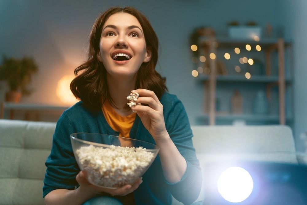 Young woman watching projector, TV, movies with popcorn in the evening.