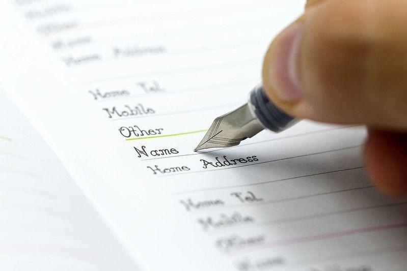 A person writing the name on a paper with a pen.